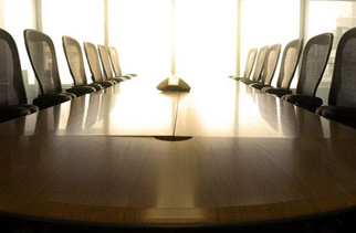 Picture of a long table with lots of chairs around it in a boardroom.