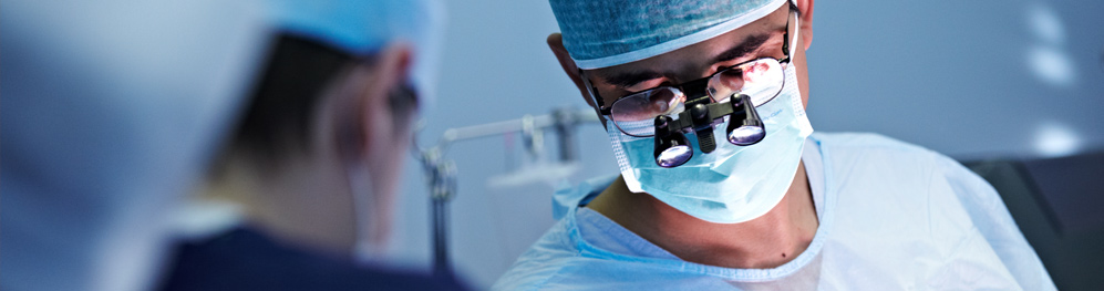 Banner picture of a male surgeon looking down at patient whom he is operating on.