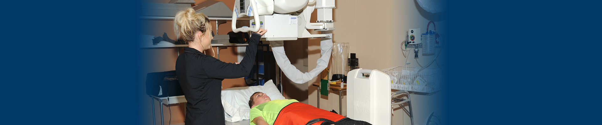 Banner picture of a female Nurse putting an X-Ray machine over a young male patient that is laying on his back with his head resting on a pillow.