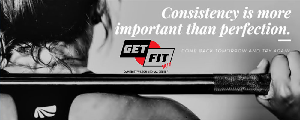 Banner picture of the back of a woman's shoulder and head. She is holding a weight up above her head. Banner says:

Consistency is more important than perfection.
COME BACK TOMORROW AND TRY AGAIN

GET FIT 24/7
OWNED BY WILSON MEDICAL CENTER