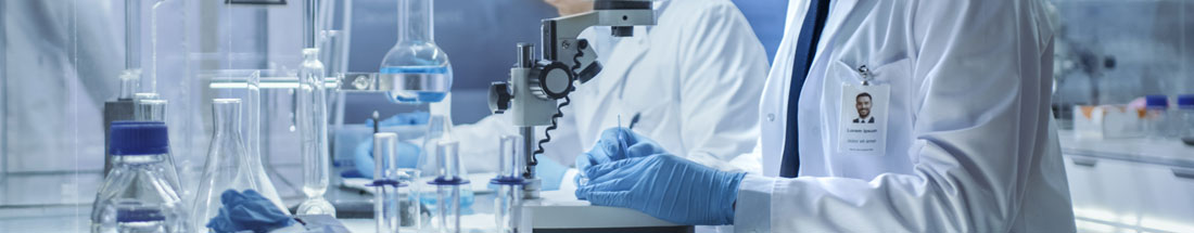 Banner picture of two Laboratory workers in a Lab. There is test tubes and lab equipment. One man is holding a microscope