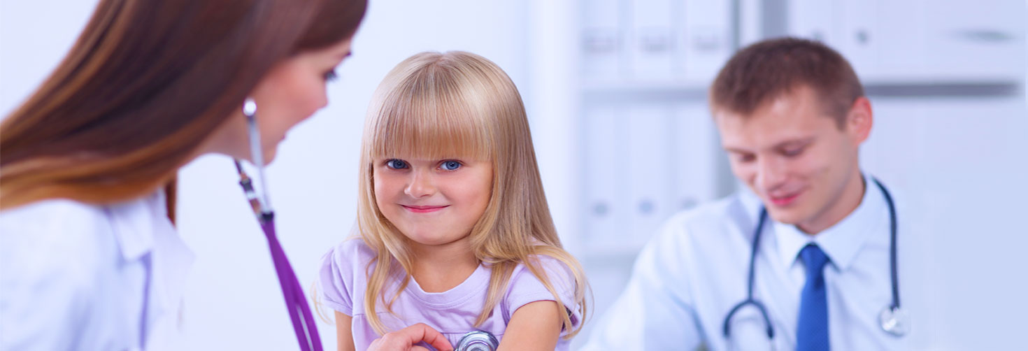 Banner picture of a female Physician listening to a little girls heart beat with a stethoscope. There is a male Physician in the background and he is smiling.