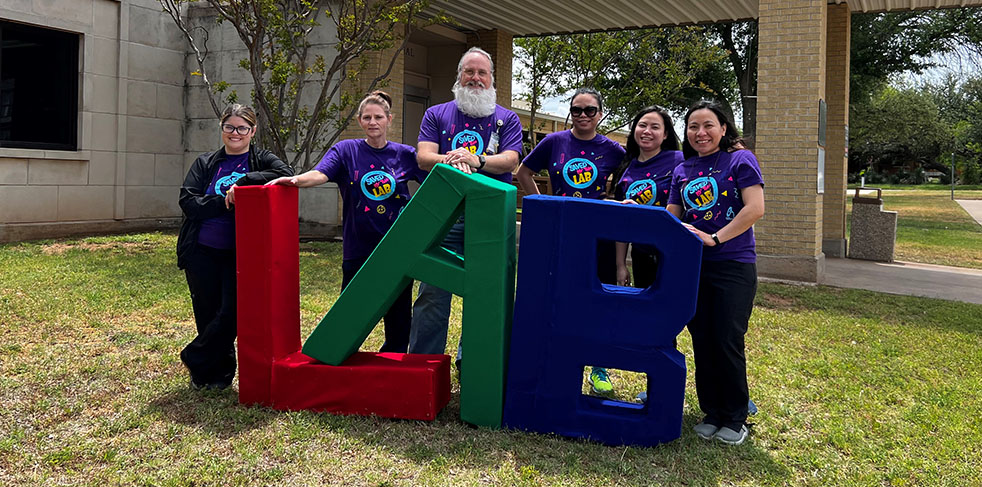 LAB workers standing behind big letters that read "LAB" outside of the Hospital.