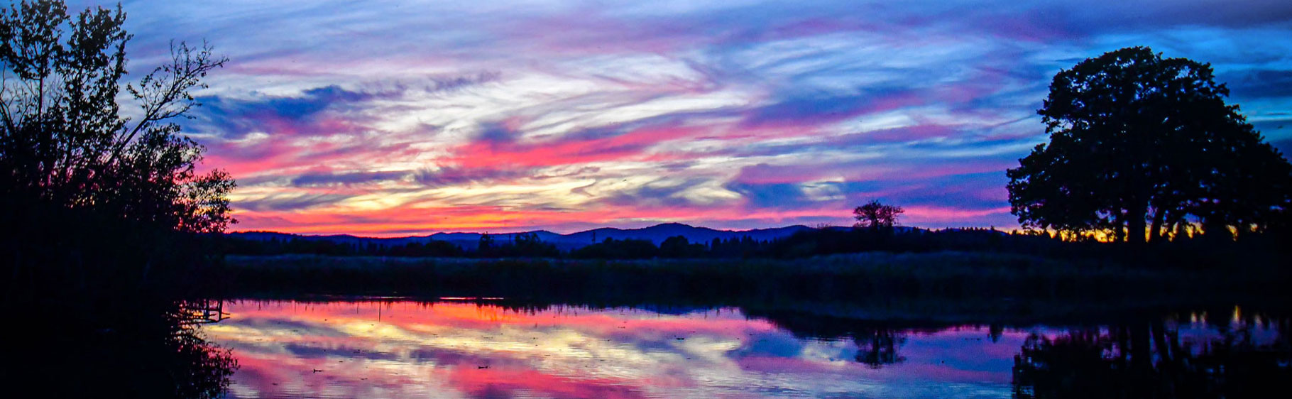 Banner picture of a beautiful sunset over a lake. There is a reflection on the water of the clouds.