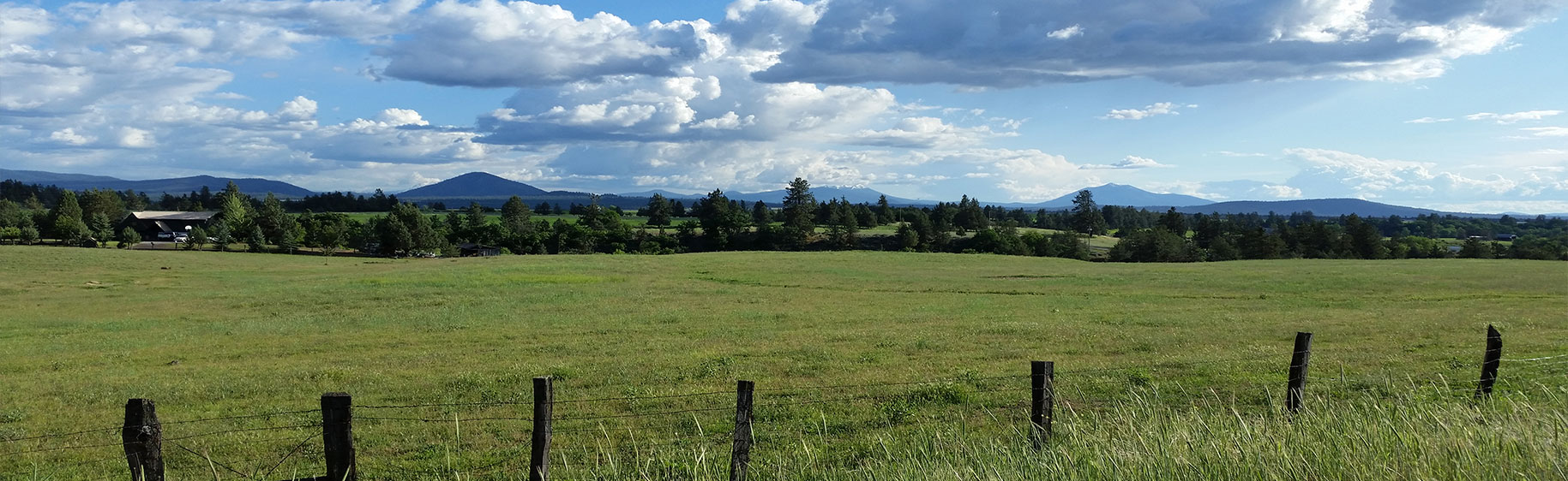 Banner picture of a large piece of land fenced. There is trees and mountains in the distance and lots of clouds in the sky.