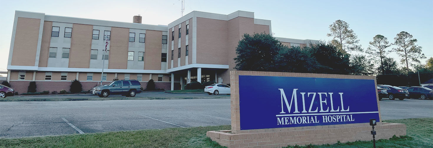 Banner picture of an outside view of the Mizell Memorial Hospital with cars parked in the parking lot.