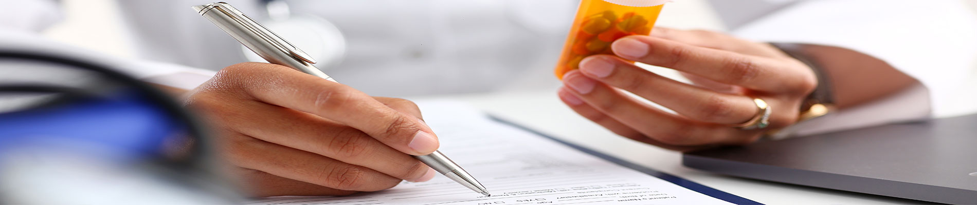 Physician holding a pill bottle while writing out a prescription refill
