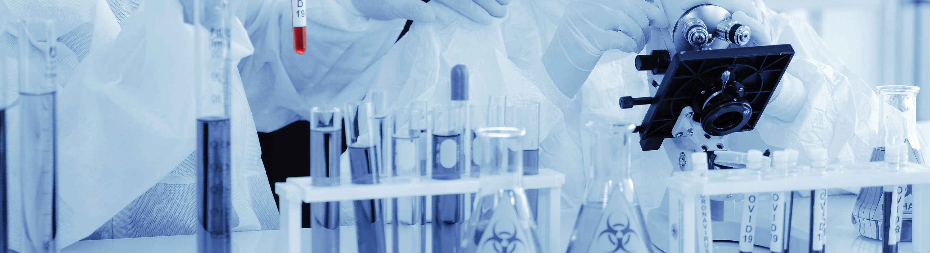 Banner Picture of a Laboratory. There is test tubes, lab equipment, and hands in gloves touching a Microscope