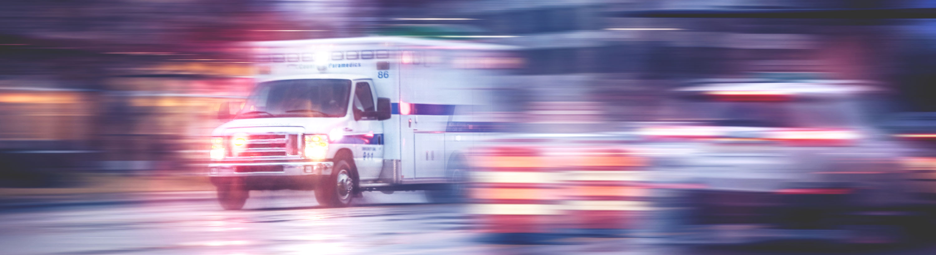 Banner picture of an ambulance in motion on the road with their lights on.