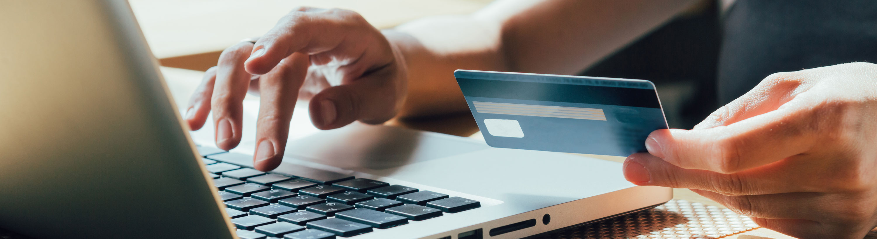 Banner picture of a man holding a debit card in one hand and his other hand is on the keyboard of his open laptop.