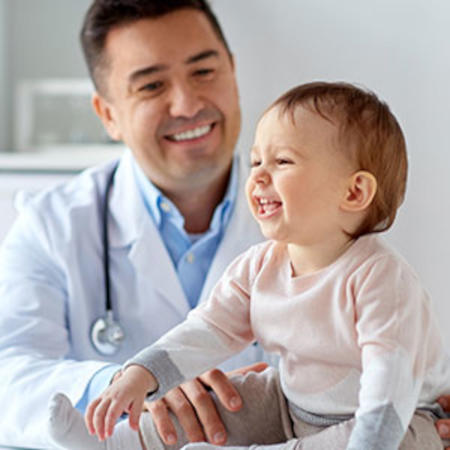 Banner picture of a male Physician holding a baby girl. They are both smiling.