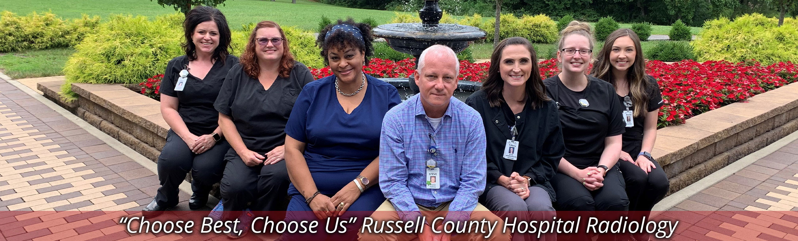 Banner Picture of our Radiology Staff sitting outside in front of a water foundation that is surrounded by beautiful flowers. There is one male and  six females. Banner says:
"Choose Best, Choose Us" Russell County Hospital Radiology