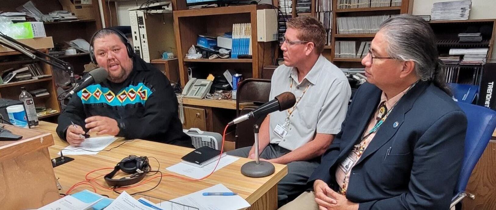 Banner picture of three males sitting down in a Radio Station in front of microphones. One man is talking with headphones on and there is two Guest sitting next to him.
Radio Program