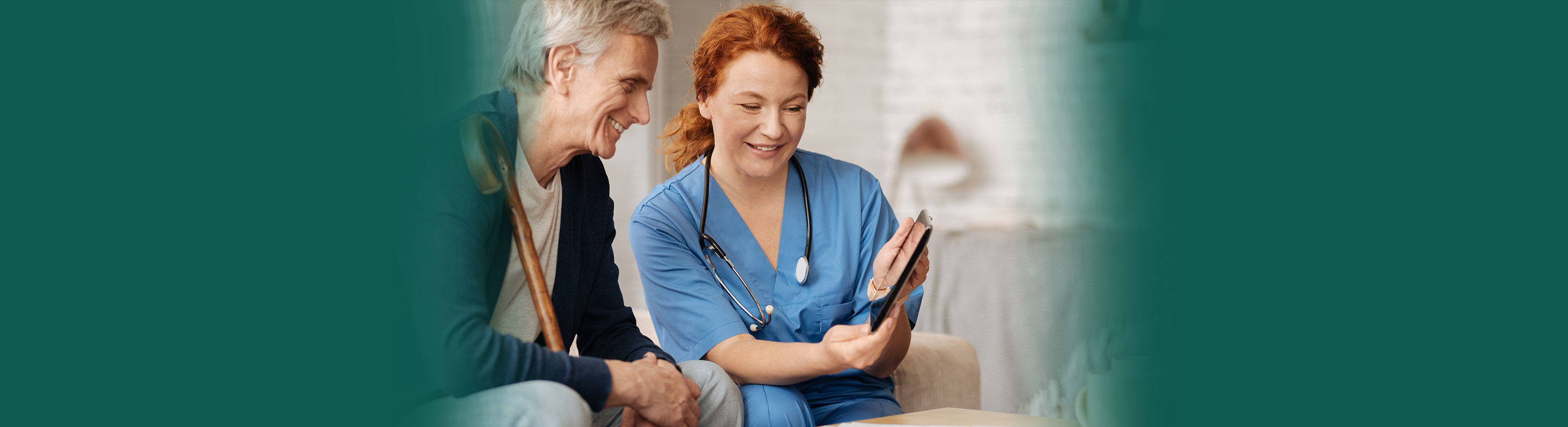 Banner picture of a female Nurse sitting down next to a male patient. They are looking down at a tablet and smiling.