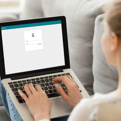 Picture of a female sitting on a couch with an open laptop showing a username and password box.