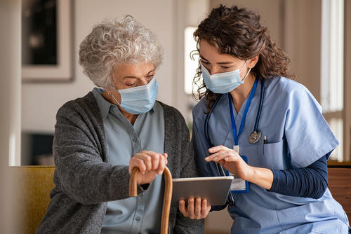 Picture of a female Nurse sitting next to an elderly female patient. They are both looking down at a smart tablet.