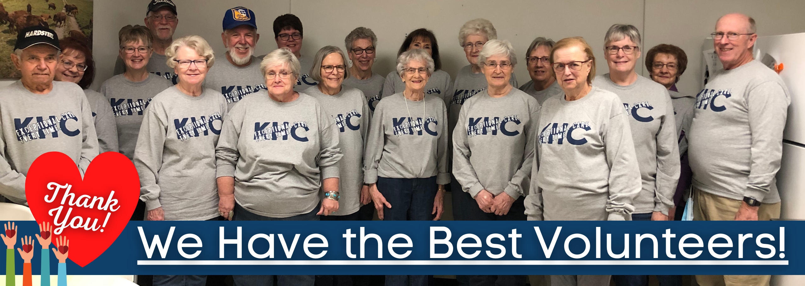 Banner picture of Kingman Healthcare Center Volunteers. 
There is a group of elderly Volunteers wearing matching long sleeve shirts that says, "KHC- EXCEPTIONAL CARE. EVERY TIME." There is 15 females and 4 males smiling.

There is a small banner across the bottom of the picture that says "We Have the Best Volunteers!" 

Graphic to the left of banner of 4 rising hands with a heart on each hand and a large heart next to the hands that says "Thank You!"