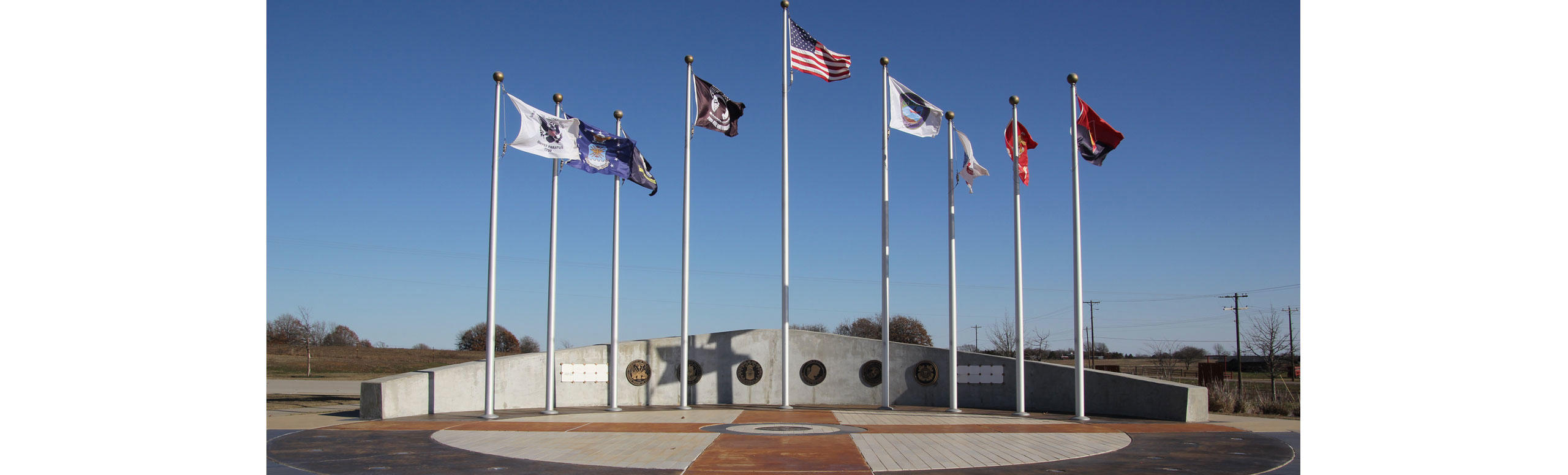 The Seminole Nation of Oklahoma- outside shot of plaques on a concrete wall and nine standing flags flying in the wind.