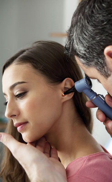 Male Medical Physician using a otoscope in a female patient's ear.