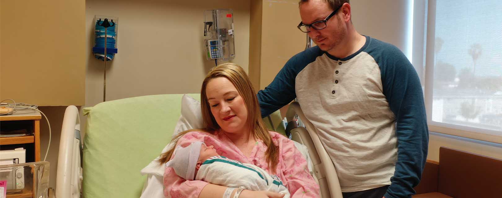 Picture of a new mom and dad with bewborn baby in their hospital room.